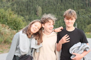 Zwei Jugendliche und eine Betreuerin schauen in die Kamera und lachen. Sie scheinen ein engen Verhältnis zu haben. Im Hintergrund sieht man einen Wald