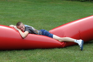 Ein Junge liegt auf einem roten Gaudiwurm und entspannt sich. Er lächelt in die Kamera