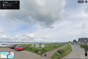 von einem Parkplatz aus ist ein Strandabschnitt mit Strandkörben und Wiese zu sehen.