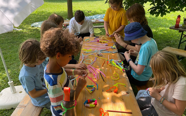 Bild zeigt Kinder bei der Freizeit 5 days, die draußen an einem Tisch sitzen und basteln.