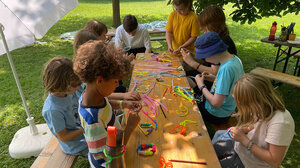 Bild zeigt Kinder bei der Freizeit 5 days, die draußen an einem Tisch sitzen und basteln.